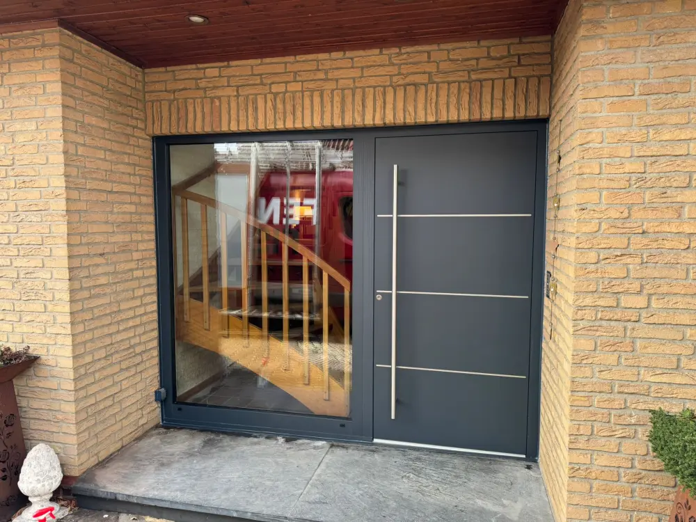 Moderne anthrazitfarbene Haustür mit Edelstahl-Applikationen in einem Klinker-Eingangsbereich